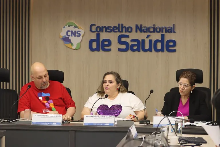 Mesa composta por Get&uacute;lio, Fernanda e Eliane. Ao fundo logomarca do CNS